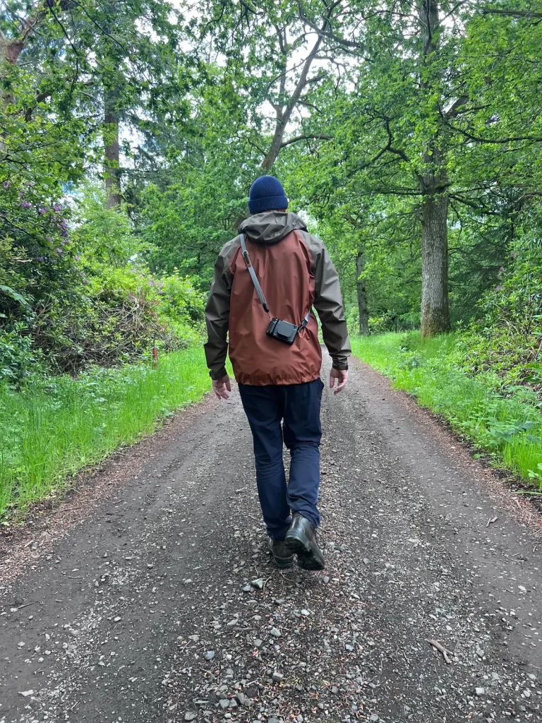 A photographer walking in Scottish woodland with the Fujifilm X100VI slung over his back on a Peak Design camera strap.