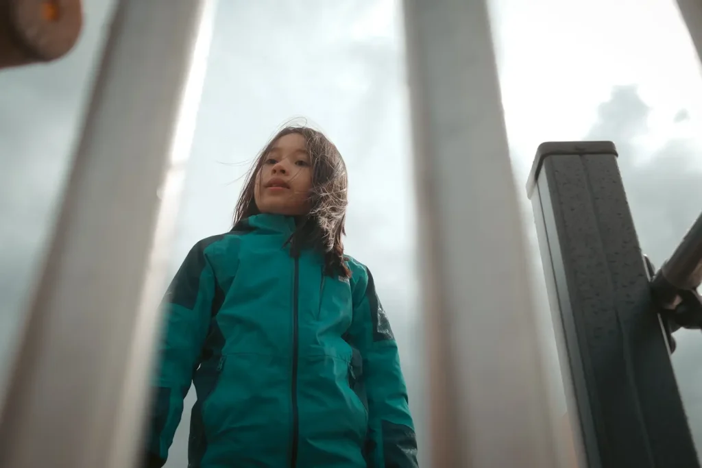 A young girl standing between metal bars in a playground. Photo is taken on the Fujifilm X100VI.