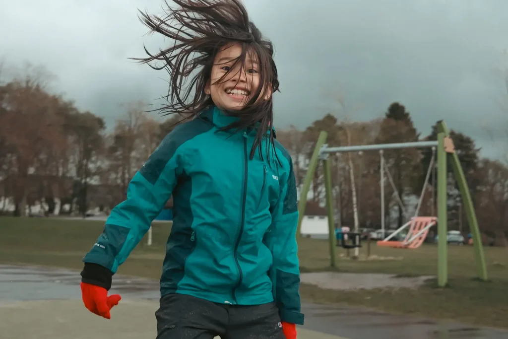 A young girl jumping for joy in a playground. Photo is taken on the Fuji X100VI and shows it is capable of photographing fast moving children.
