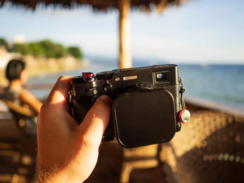 The Fujifilm X100VI held in hand in a beach bar in the Philippines with the sea in the background.