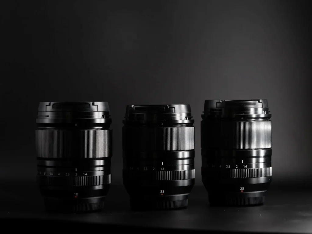 3 Fuji Prime lenses photographed together on a black background in dramatic light.