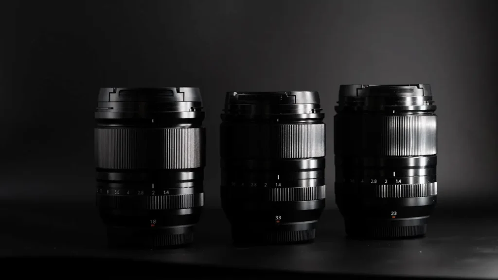 The Fuji 23mm 1.4WR lens shot on a black background next to the Fuji 18mm 1.4WR and 33mm 1.4WR lenses to show a comparison of their size.