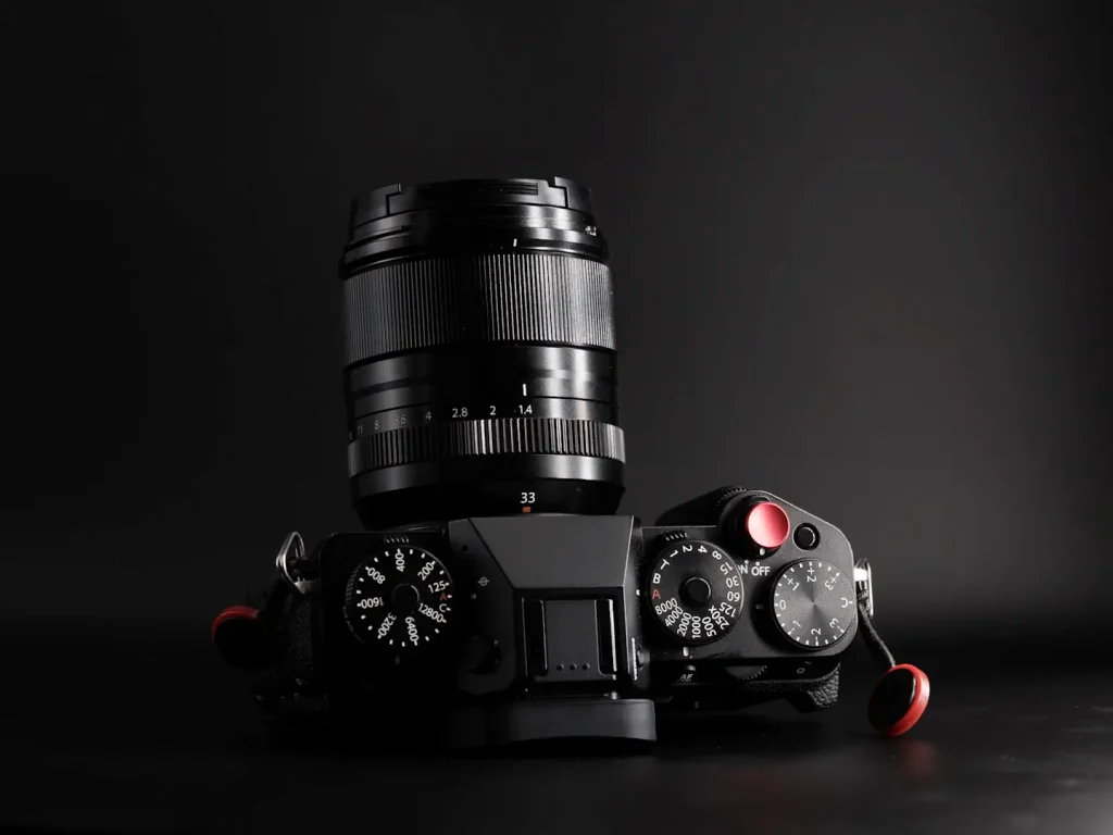 The Fuji X-T5 camera with the Fujifilm 33mm 1.4Wr lens attached, photo taken on a black background with dramatic lighting. 