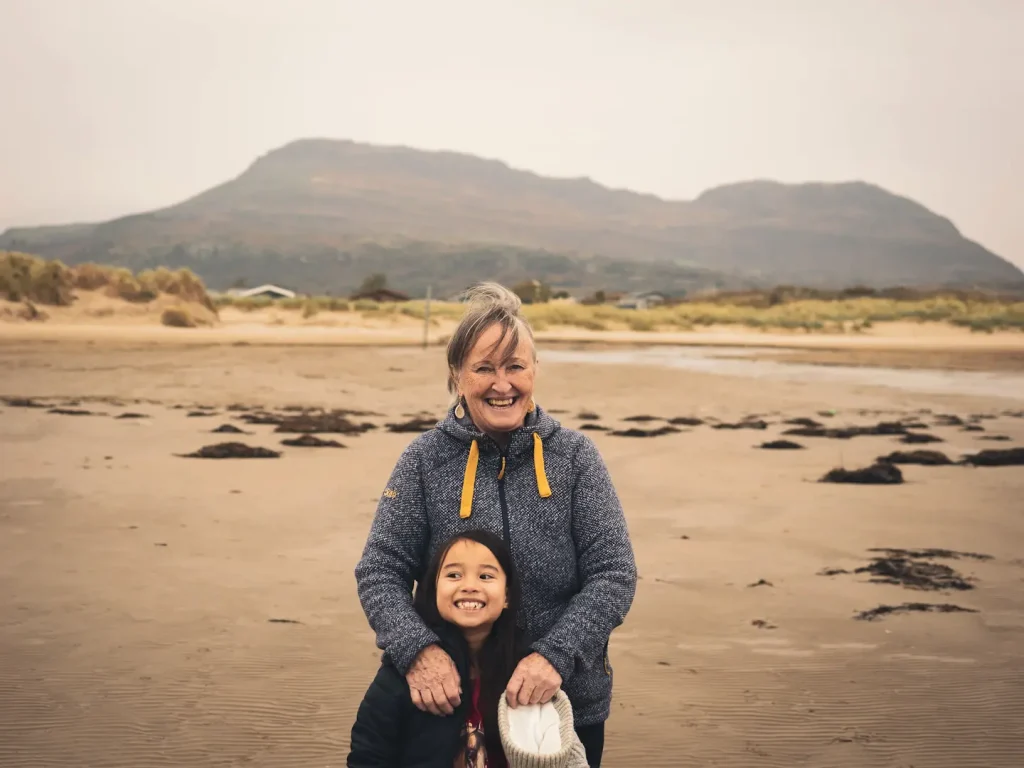 a young girl and her grandmother pose for a photo at the beach in Wales. 