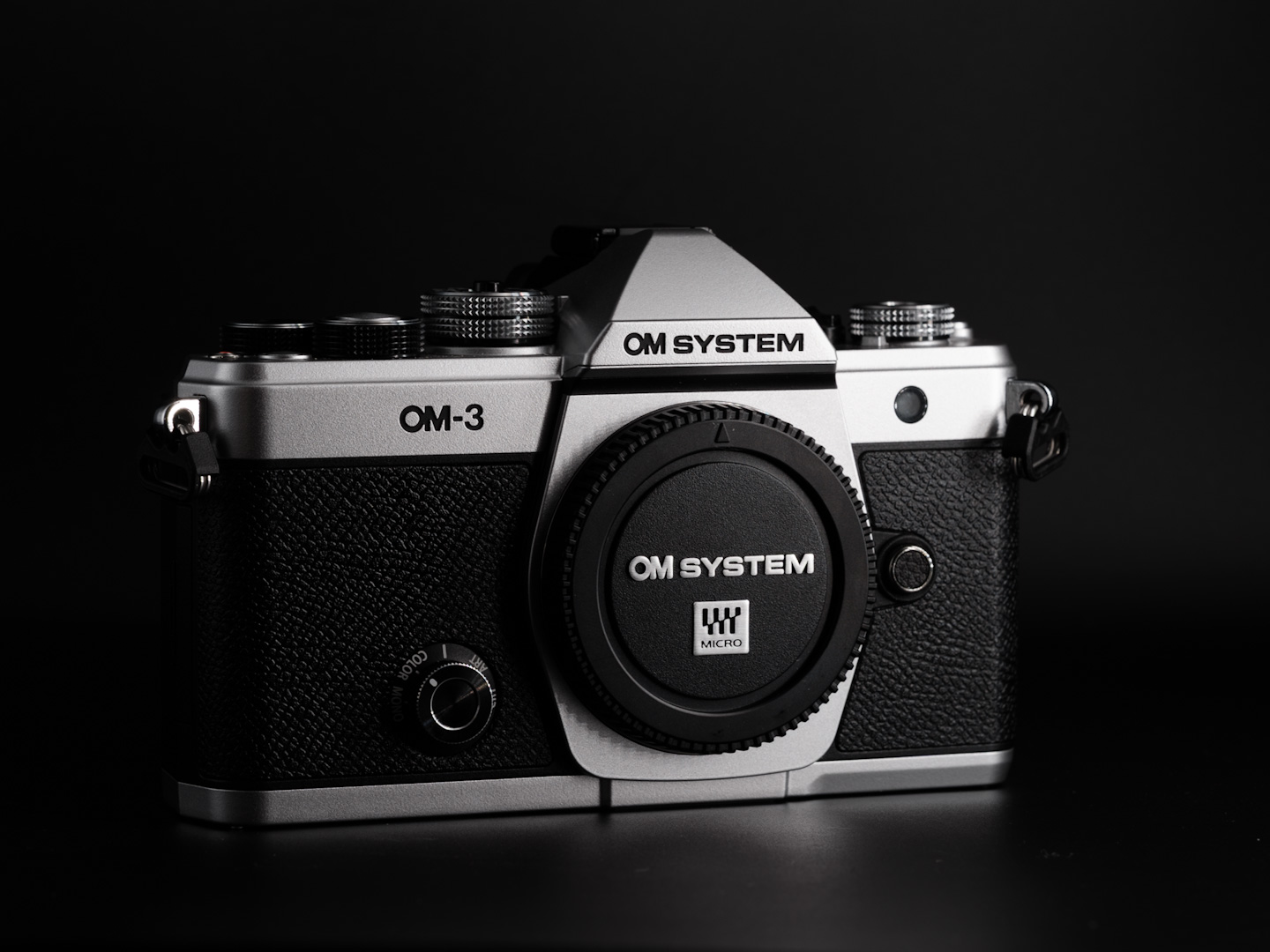 The OM Systems OM-3 camera photographed from the front on a black background in dramatic lighting.