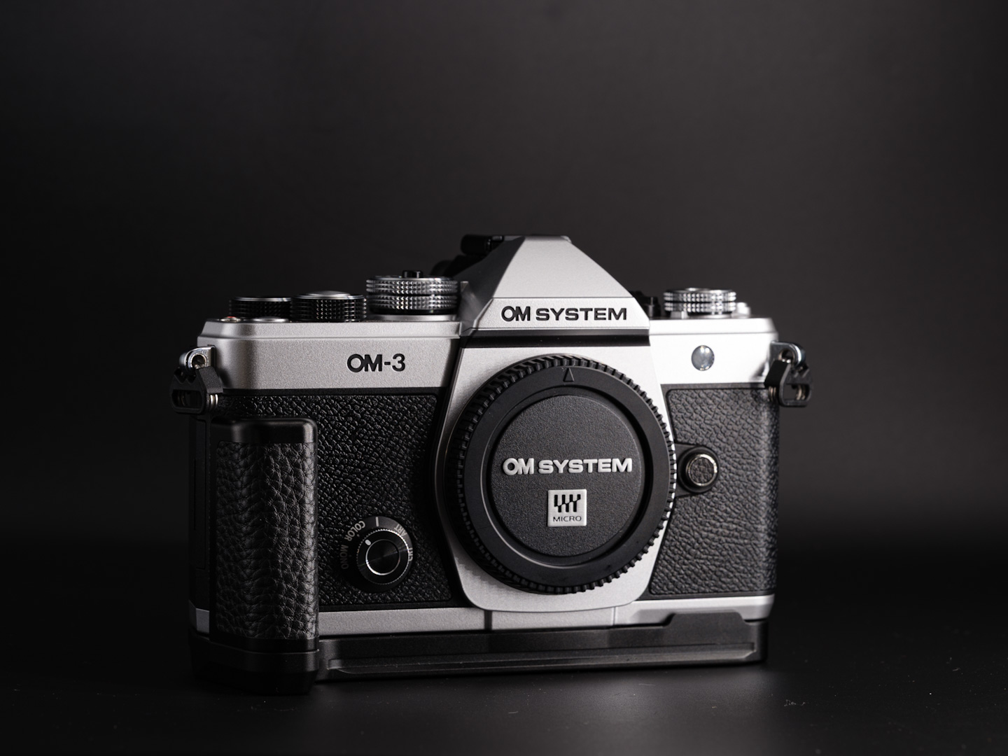 Om Systems OM-3 camera body with the Haoge L grip attached. Photographed on a black background with dramatic lighting.