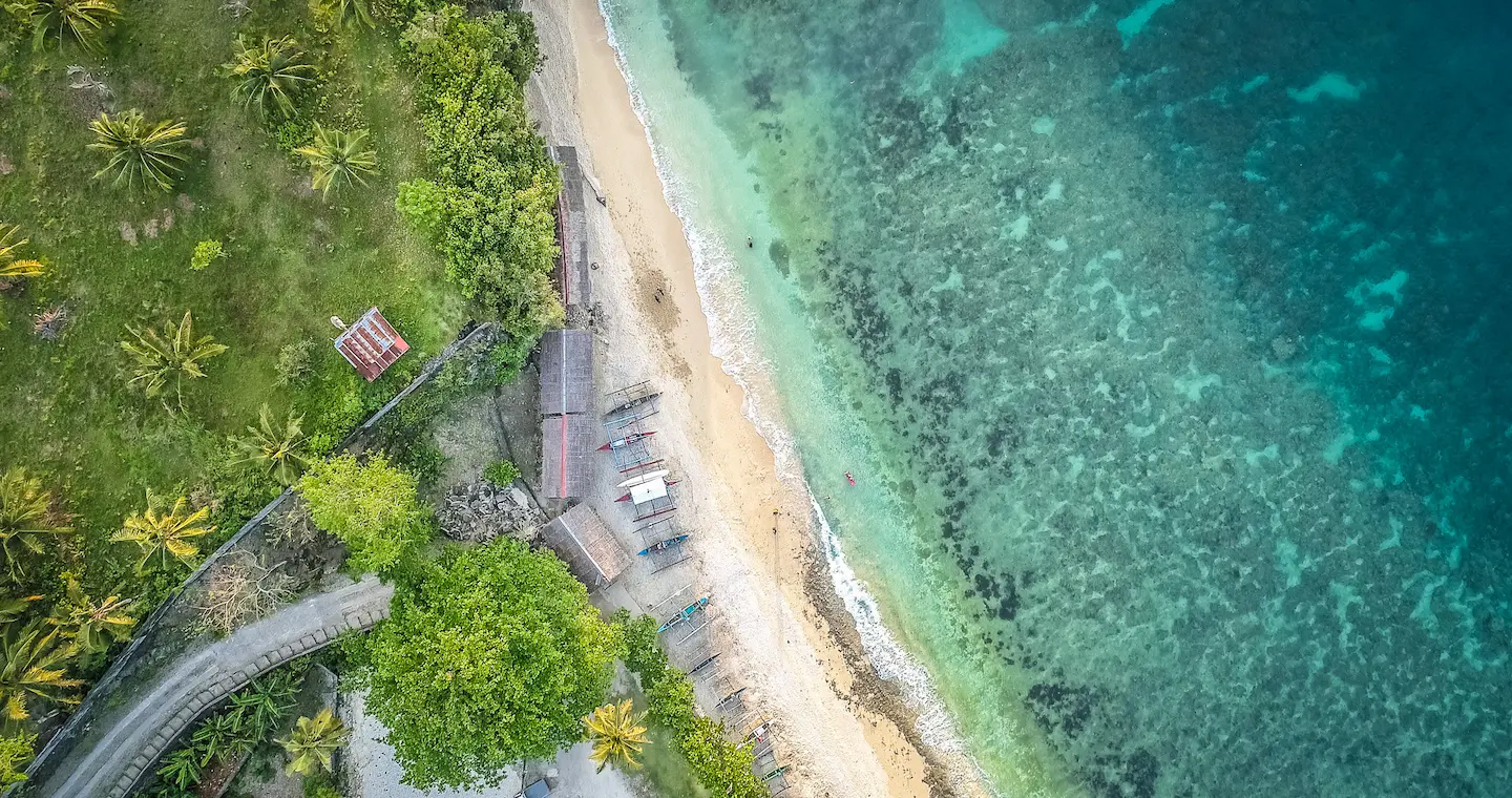 Overhead shot of a beautiful tropical beach in the Philippines showing coconut trees, white sand and turquoise sea.