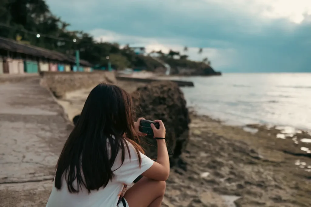 A photograph of a 9 year old girl at the seaside in the Philippines using a Ricoh GRIIIx camera to take photographs. This photo was taken on the Fujifilm 18mm 1.4WR lens. 