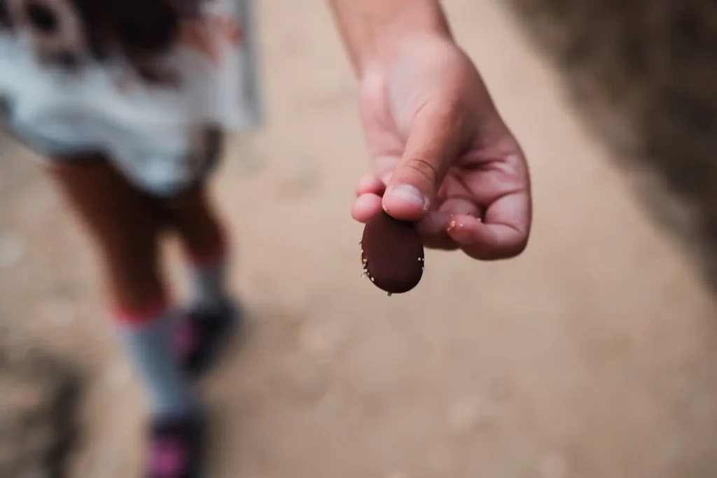 A young girl holds a beach pebble in her hand. The photo is shot with a large aperture and so the background quickly falls out of focus. 