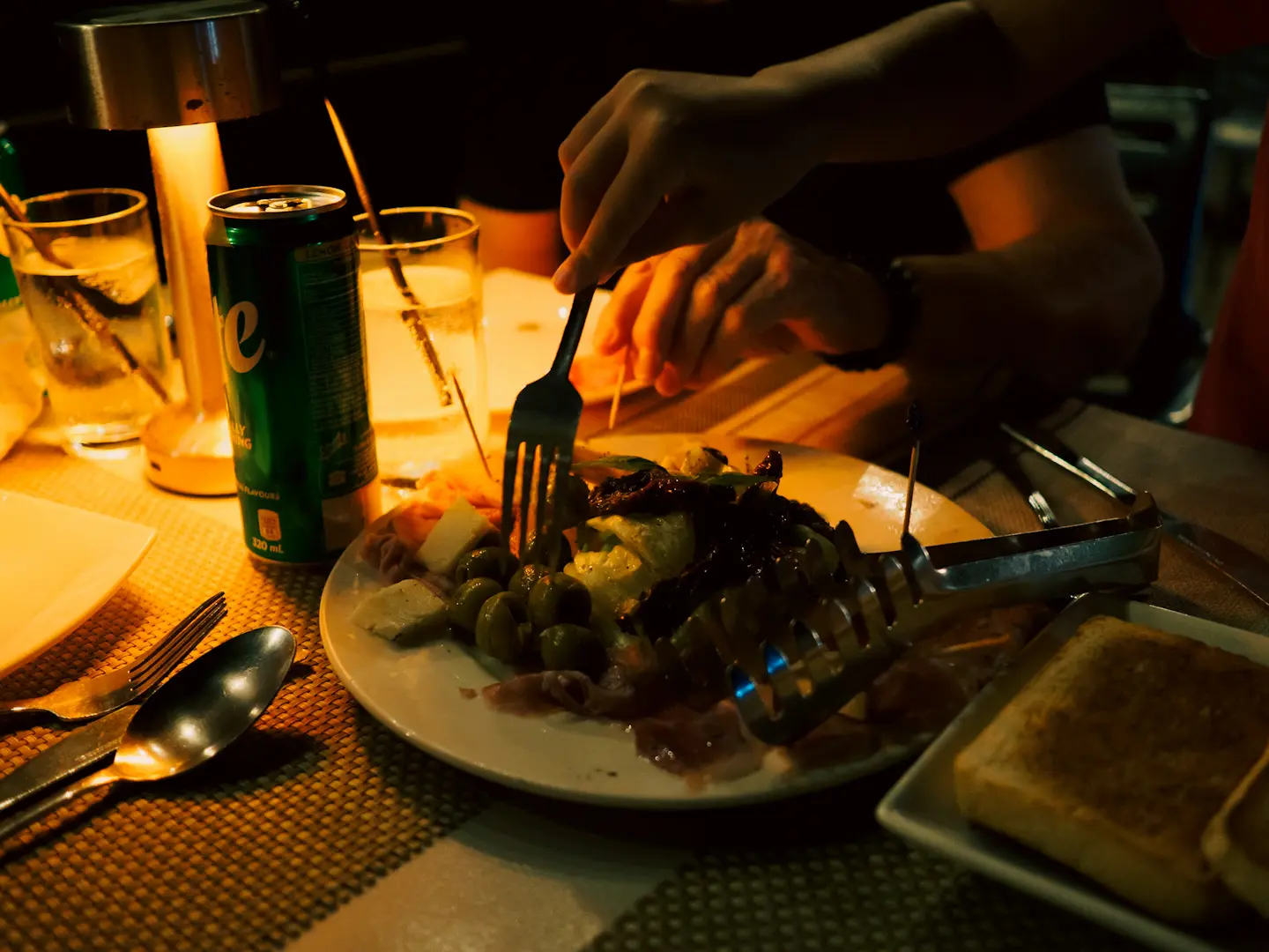 People's hands reaching for food lit only by candlelight.