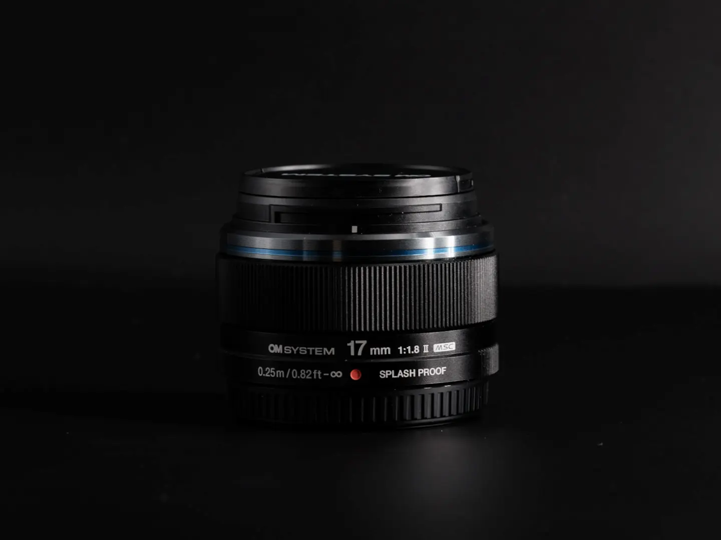 Om Systems 17mm f/1.8 mark II lens photographed on a black background in dramatic lighting.