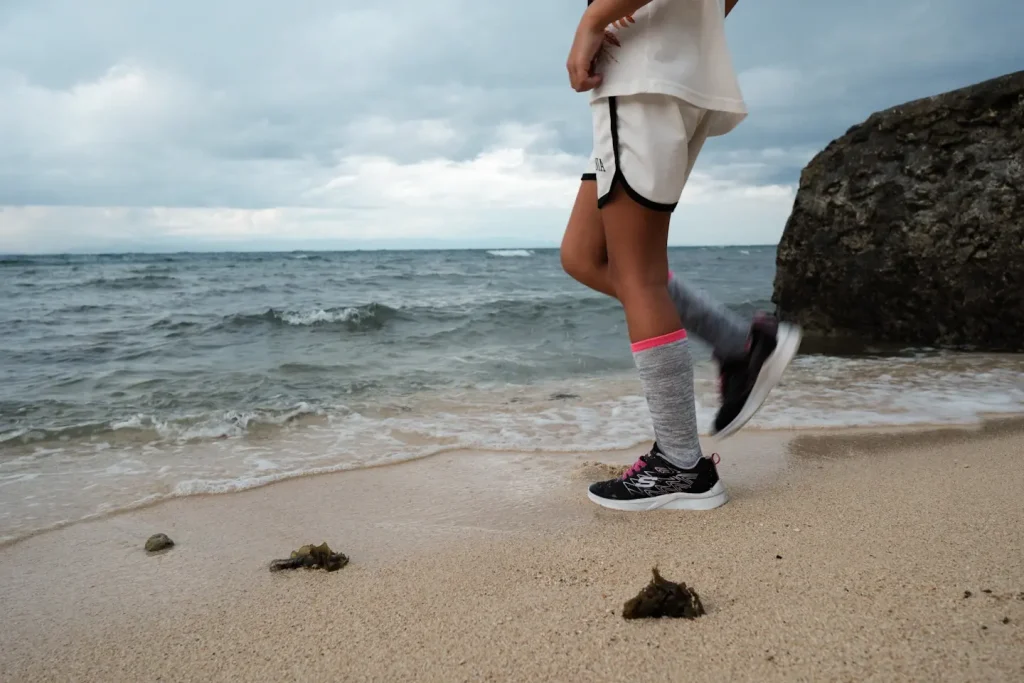 A photo of a young girl only shown from the bottom half, at the water's edge on a beach as the sea washes in towards her. Photo taken on the Fuji X-T5 and Fuji 18mm 1.4WR lens as 
