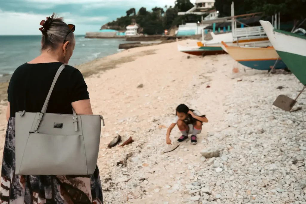 A lady and her grandaughter at the local beach in Barili, Cebu Philippines. The child is crouched down looking at shells while the grandmother walks towards her. Photo is taken on the Fuji XT5 + 18mm f/1.4WR lens. 