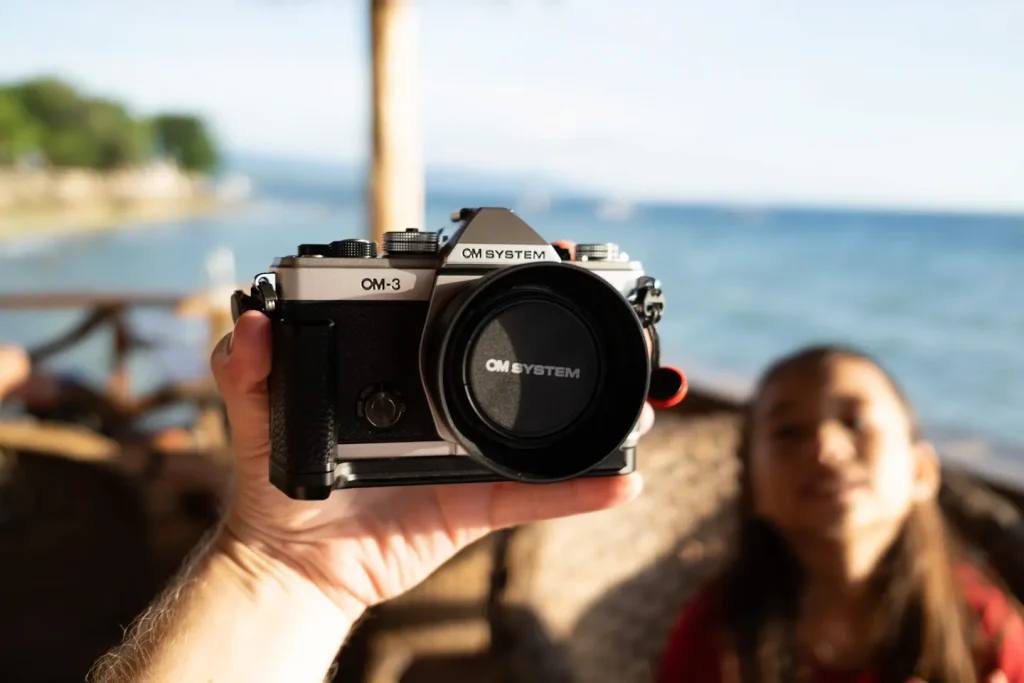 The OM Systems OM-3 camera held in a hand at a bar near a tropical beach in beautiful afternoon sun light.