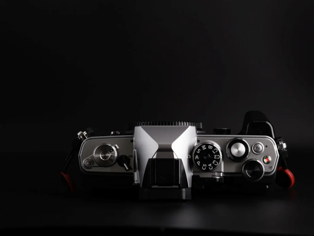 OM System OM-3 camera showing the top view including the dials with the Haoge camera grip attached. Photographed on a black background.