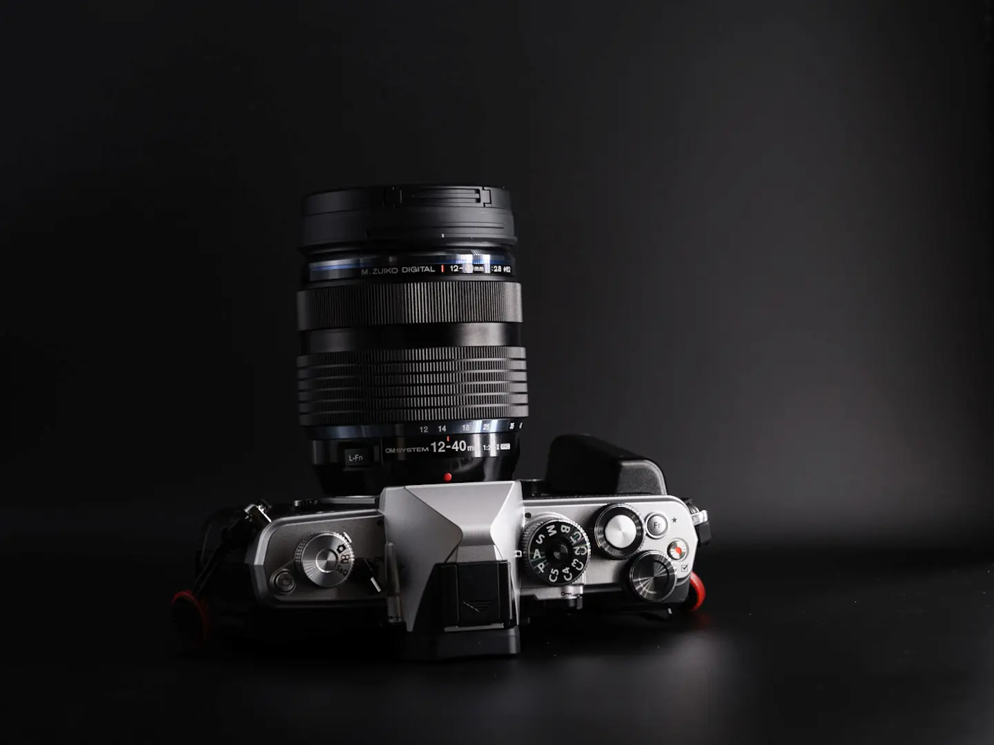 Om System OM-3 camera with the OM 25mm 1.2 pro lens attached showing the top view of the camera. Photo taken on a black background.