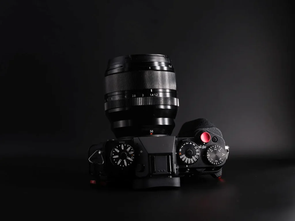 The Fuji 56mm 1.2 WR lens mounted on the Fujifilm X-T5. This view shows the top view of the camera and how far the lens protrudes from the camera body. The image is taken on a dark background.