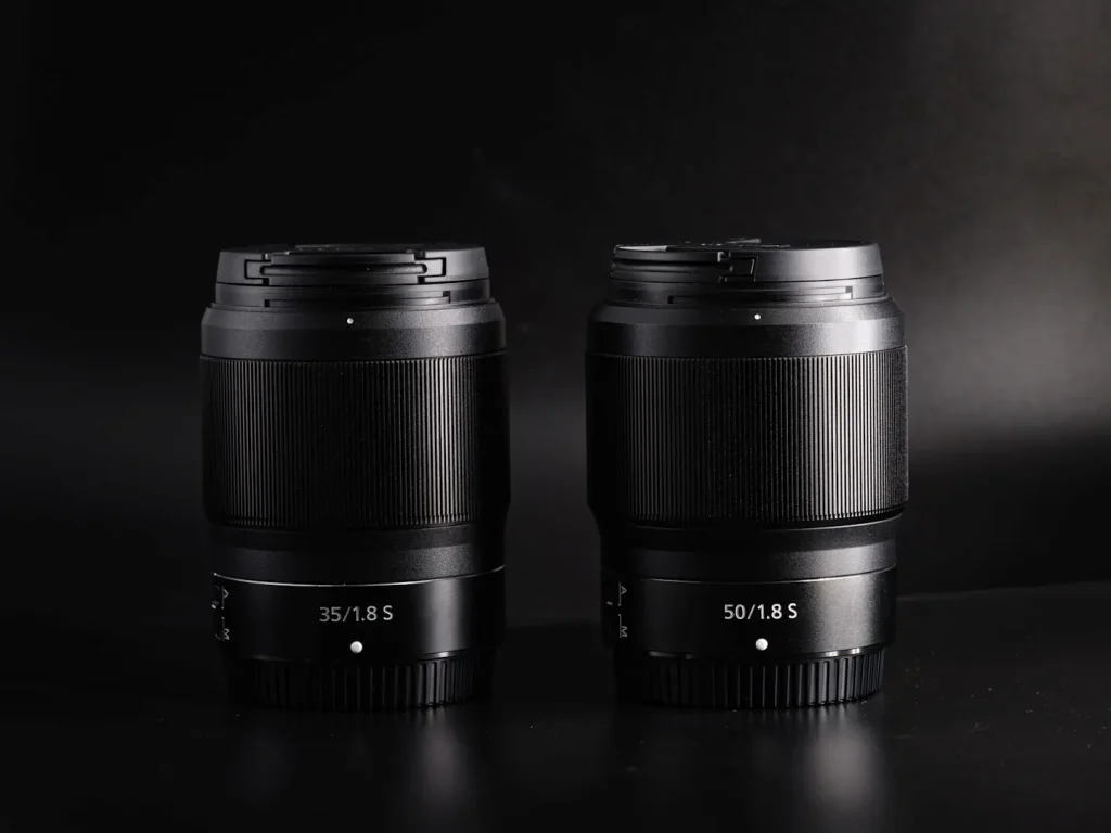 Nikon Z 35mm 1.8S and Nikon Z 50mm 1.8S lenses next to each other on a black background.