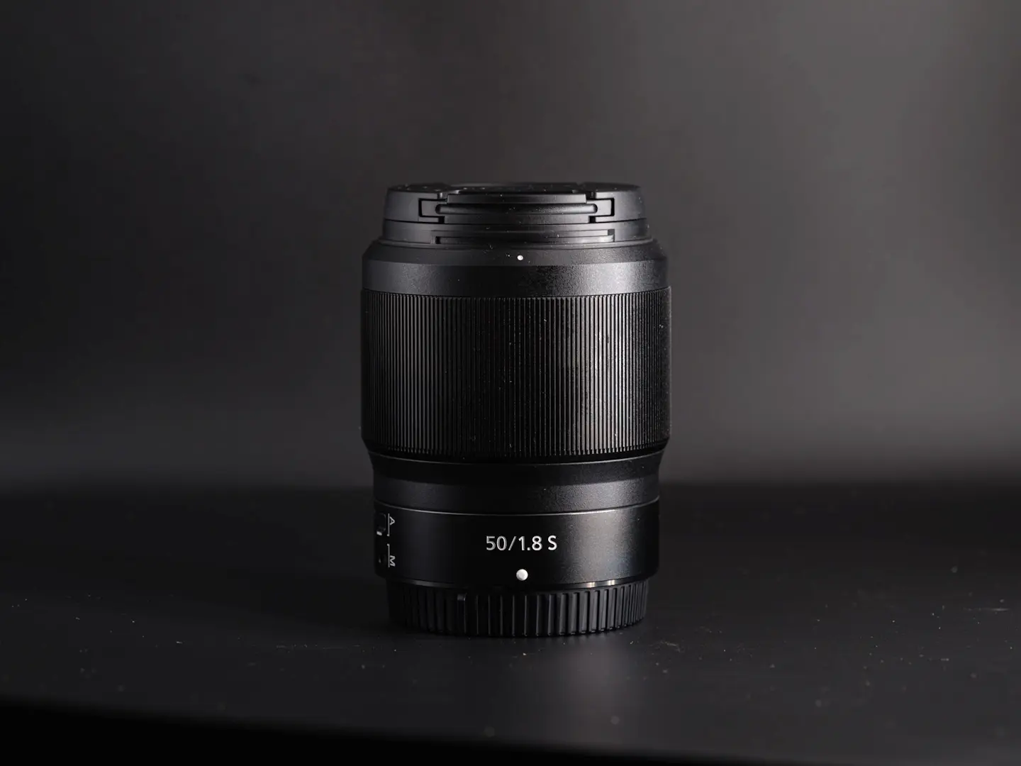 The Nikon Z 50mm 1.8S lens on a black background photographed in side light.