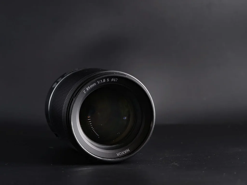 Nikon Z 85mm f/1.8S lens photographed on a black background with the front lens element visible. 