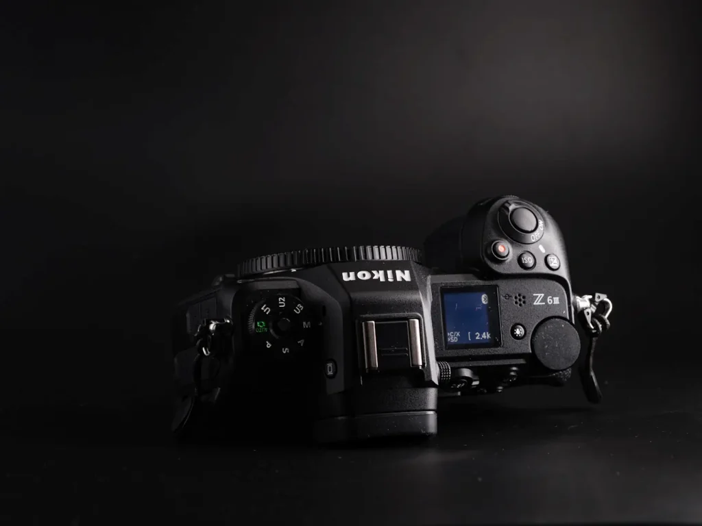 The top view of a Nikon Z6III cameras showing the top dials, LCD screen and button layout. Photo is taken on a black background. 