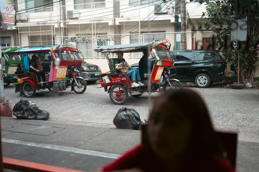 A photo of some trikes in Dumaguete city taken from inside a cafe with a young girl in the foreground. 