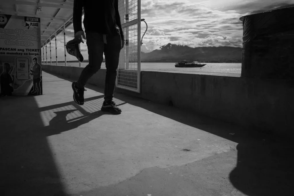 Black and white photo of a man walking down a pier in silhouette. Photo taken on the Ricoh GRIV camera.