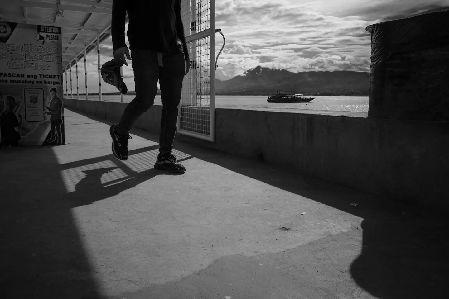 Black and white photo of a man walking down a pier in silhouette. Photo taken on the Ricoh GRIV camera.