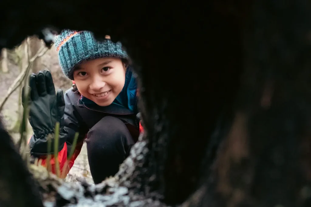 A young girl framed by a hollow in a tree smiling back towards the camera. Photo is taken on a Fujifilm X100VI camera.