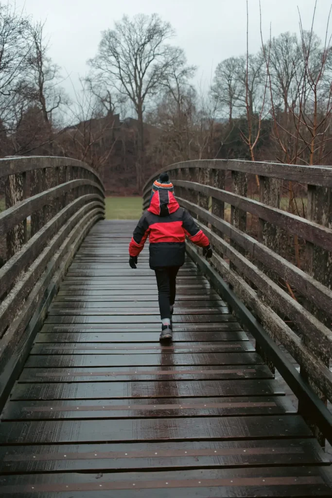 A 9 year old girl walking across a wooden bridge in a Scottish park in the rain. Her jacket is a Keela Munro junior in black and red colour. 
