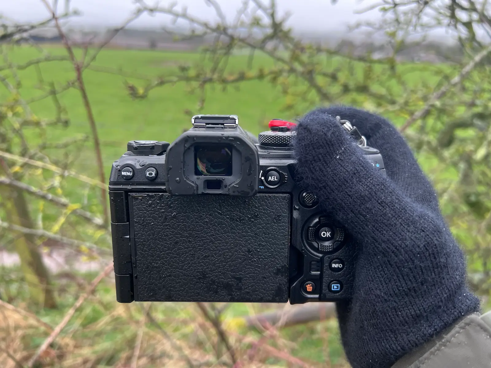 An OM System OM-1 II held in the hands of a photographer wearing gloves.