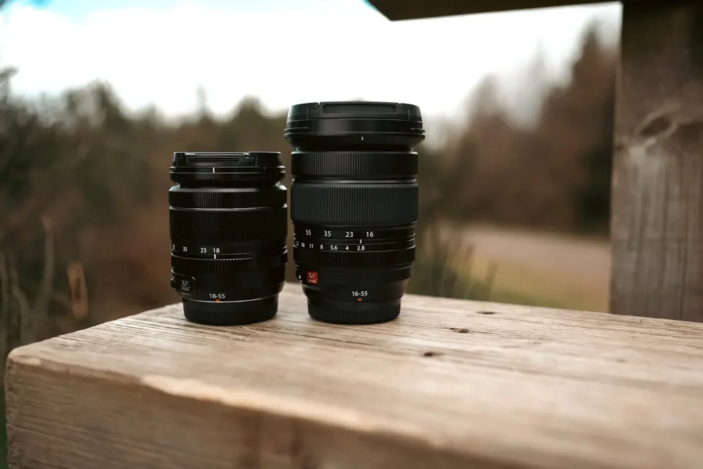 The Fujifilm 18-55mm f/2.8-4 lens next to the Fujifilm 16-55mm f/2.8 II lens on a park bench. 