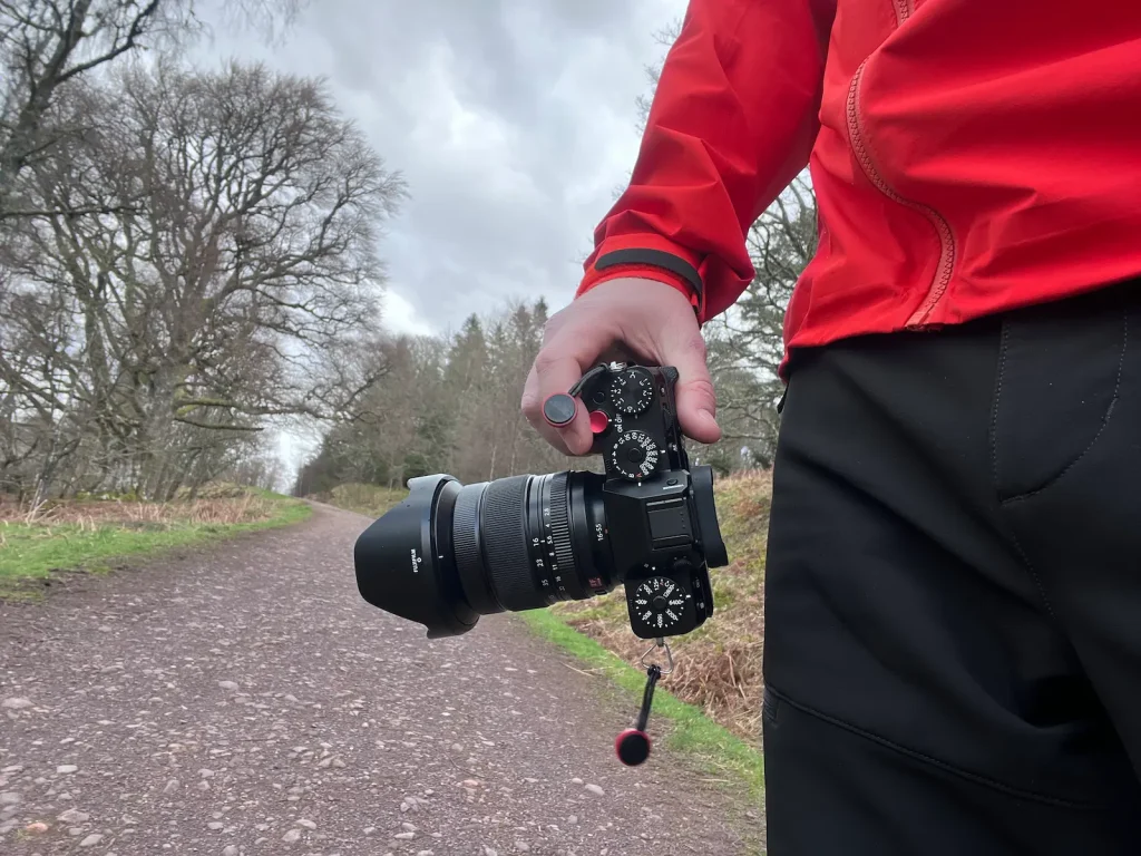 The Fujifilm 16-55mm f/2.8 II lens mounted on an X-T5 being held in a photographers hand on a walking path. 