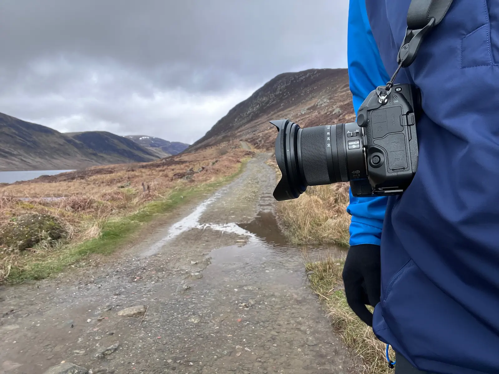 A photographer has a Nikon Z8 and Nikon Z 14-30mm f/4 hanging from a camera strap with a Scottish glen in the background.