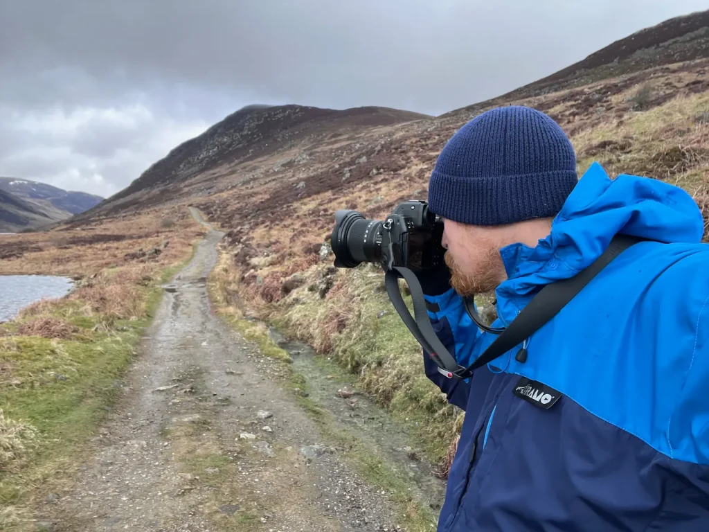 A landscape photographer dressed in a Paramo jacket in the Scottish Highlands taking photos on a Nikon Z8 and Nikon Z 14-30mm f/4 lens. 
