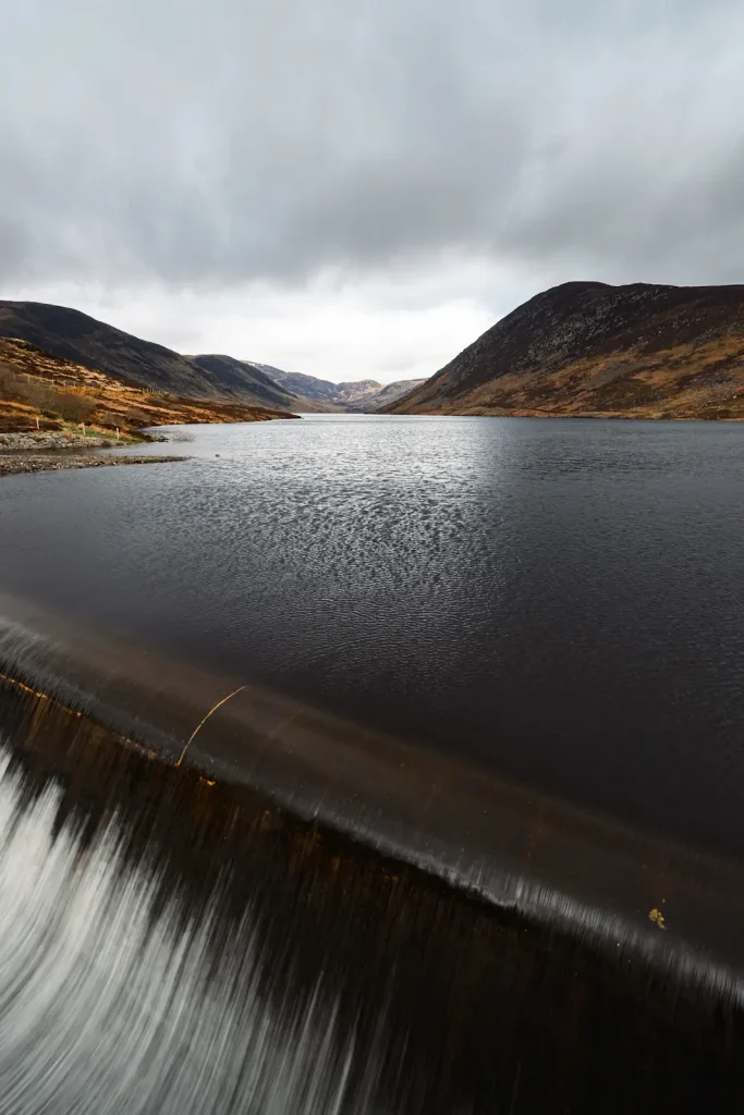 Overflow water cascading out of Loch Turret with the loch and mountains in the background. 