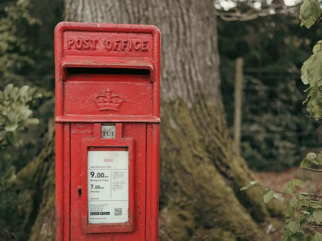a bright red post box in Scotland with trees in the background.