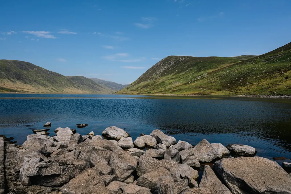 A view of loch Turret near Crieff in Scotland with shoreline rocks in the foreground and the glen and mountains behind the loch. 