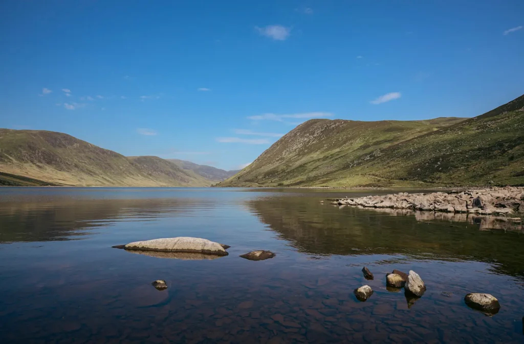A photograph of Loch Turret in the Scottish Highlands with blue sky and rocks in the water in the foreground with mountains behind. Photograph is taken on the Nikon Z8 camera with the Nikon Z 20mm 1.8S lens. 