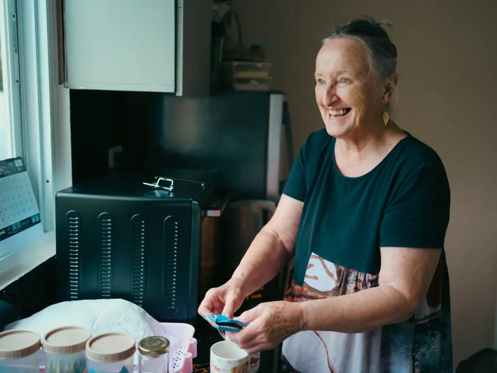 An older lady smiling as she makes a drink in the kitchen. Photo is taken on the Fujifilm GFX100S camera.