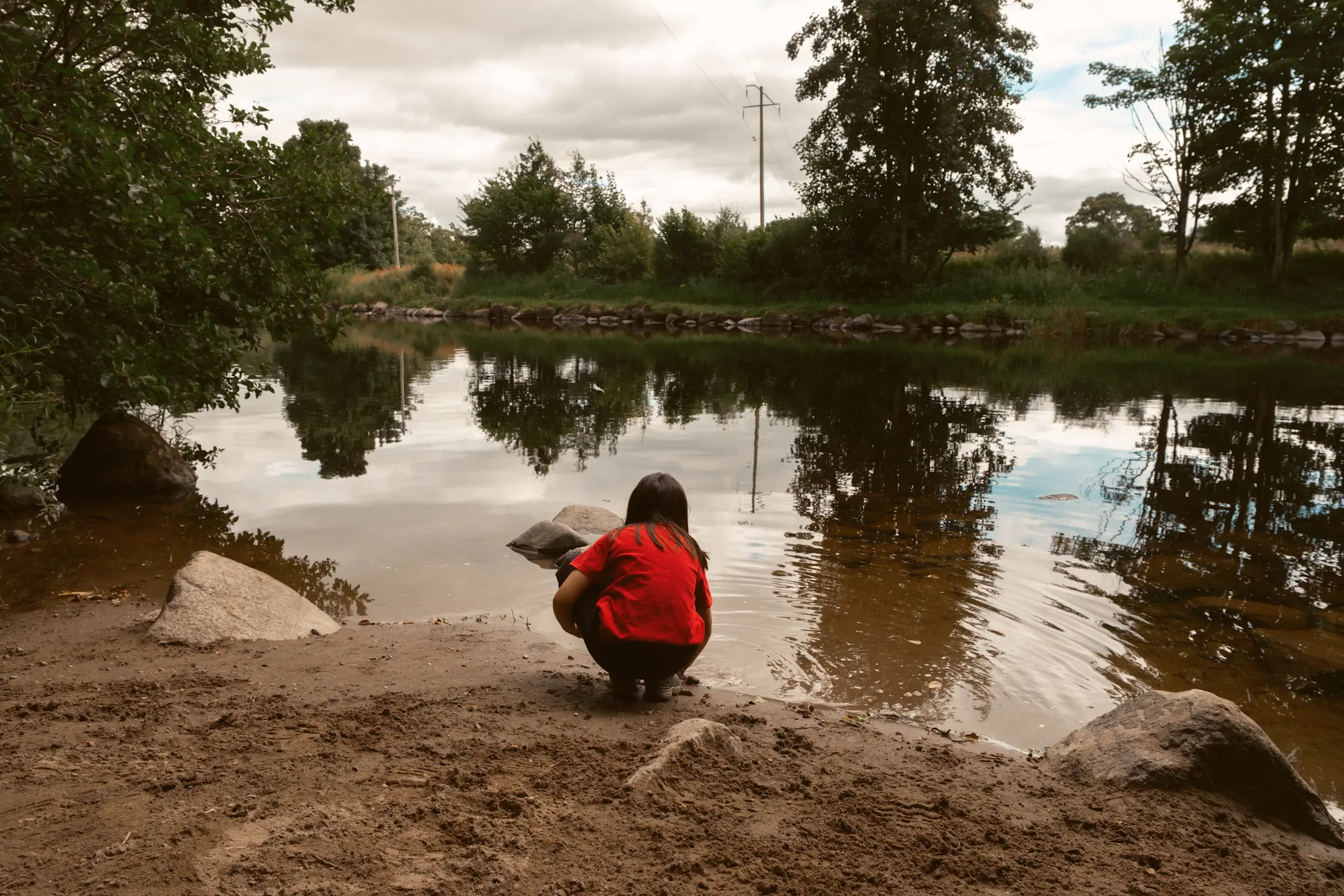 A young girl sits by a riverbank looking out to the water. This is the river Earn in Crieff, Scotland.
