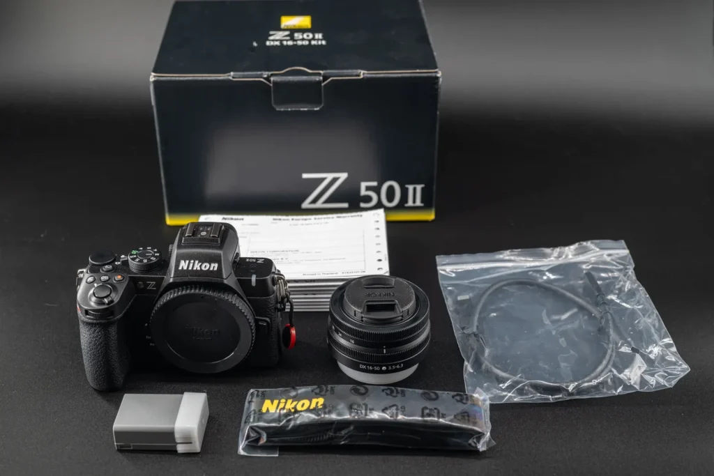 The Nikon Z50II and kit lens plus all accessories included with the camera, laid out on a black background.