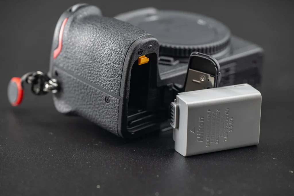 The Nikon Z50II and Nikon EN-EL25a battery photographed together on a black background in order to show the correct way to insert the battery in to the camera.