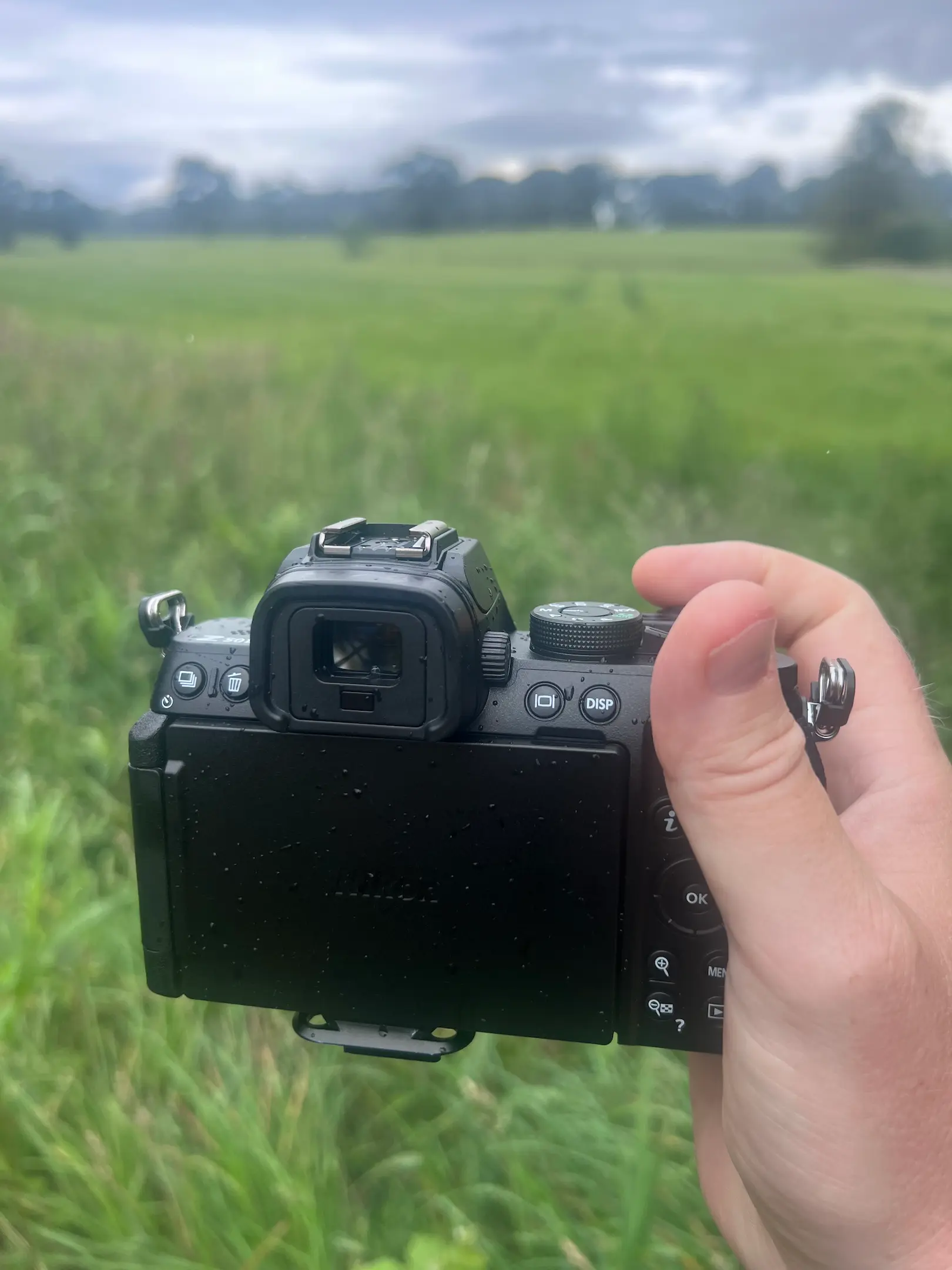 A Nikon Z50II camera shown in a photographer's hand pointing towards farmland.