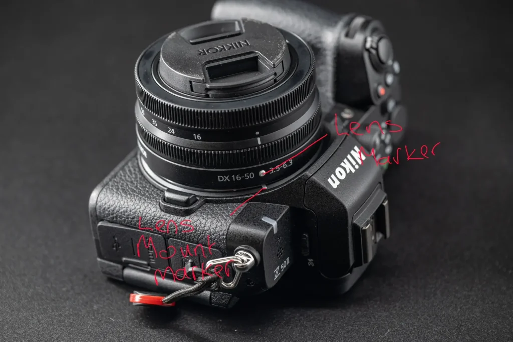 A photo of the Nikon Z50II camera that has been marked up with red writing in order to show the lens mount marker and the lens marker in order to help beginners understand how to attach a lens to the camera.