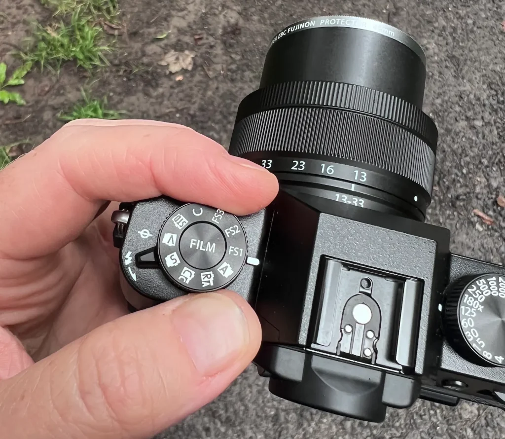 A photographer's hand adjusting the Film Simulation dial on the top of the Fujifilm X-T30 III camera.